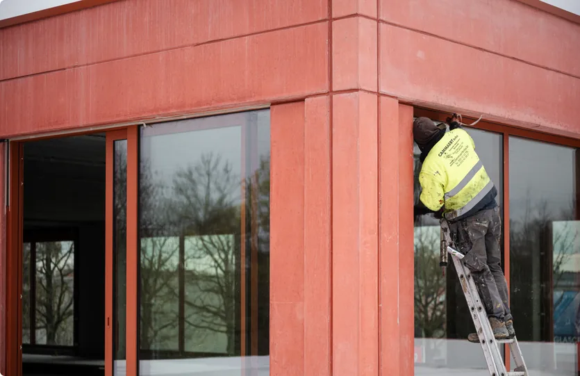 Hoek van het nieuwe gebouw in rood zichtbeton, met een kitter op de ladder